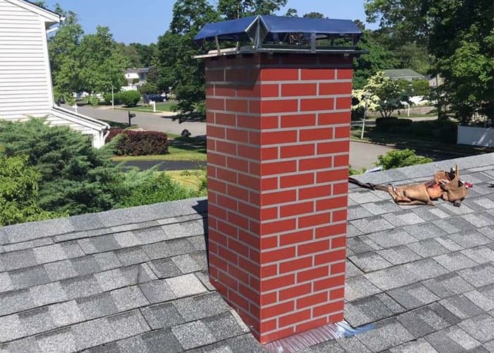 Rebuilt red brick chimney with a new metal cap on a shingle roof