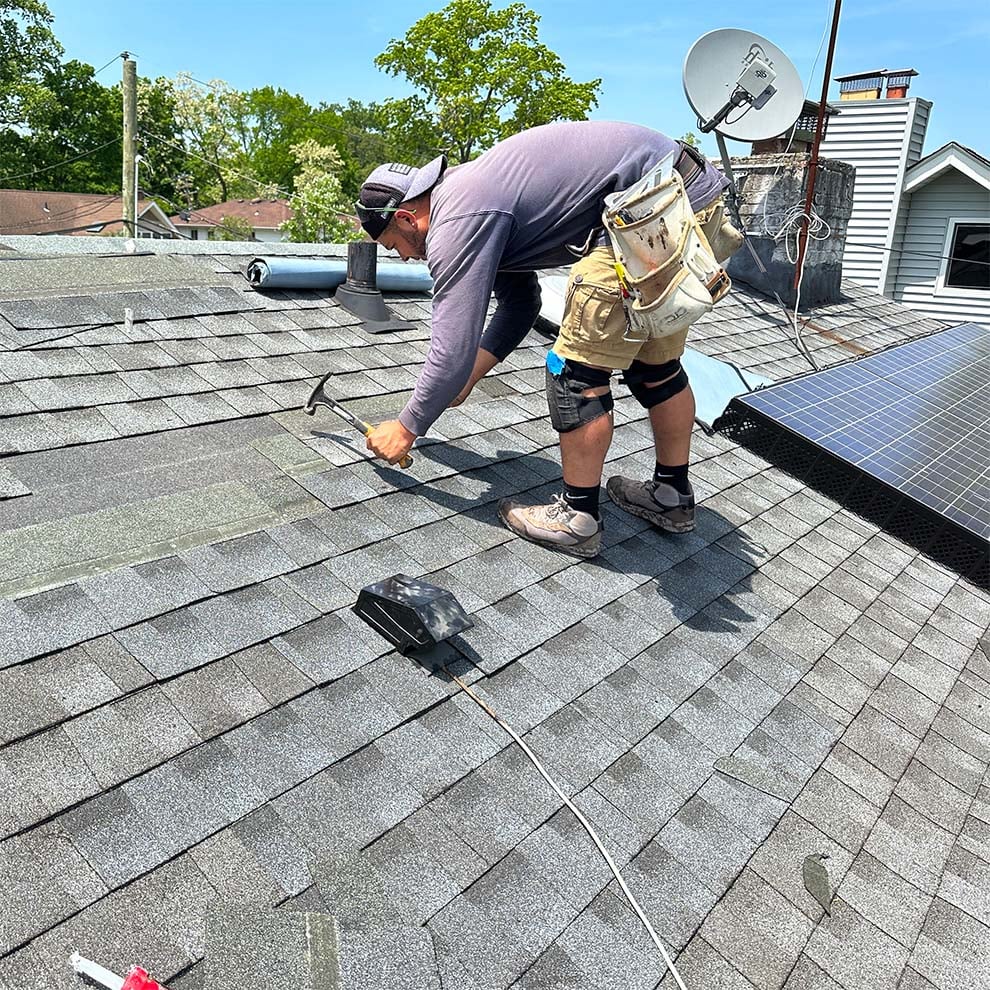 Home Crew roofer nailing down new gray shingles on a Long Island home