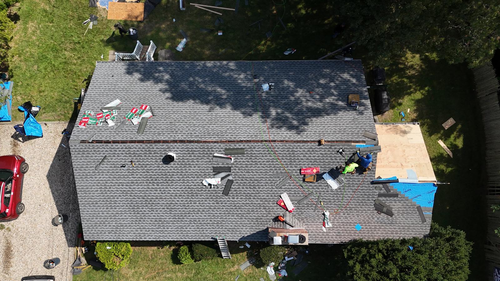 Two Home Crew roofers installing new asphalt shingles over fresh decking, seen from above