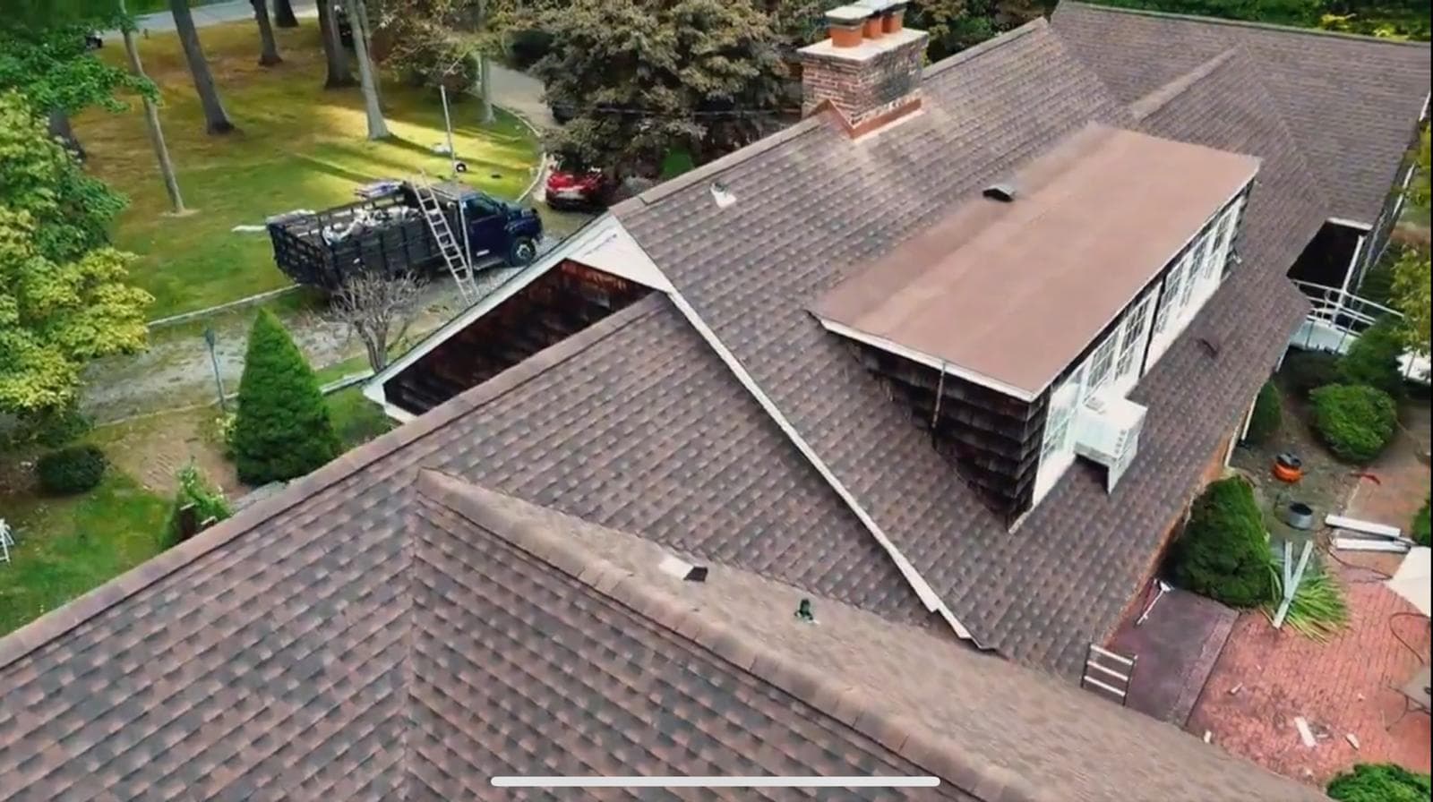 Aerial view of a brown shingle roof with a brick chimney and a low-slope section