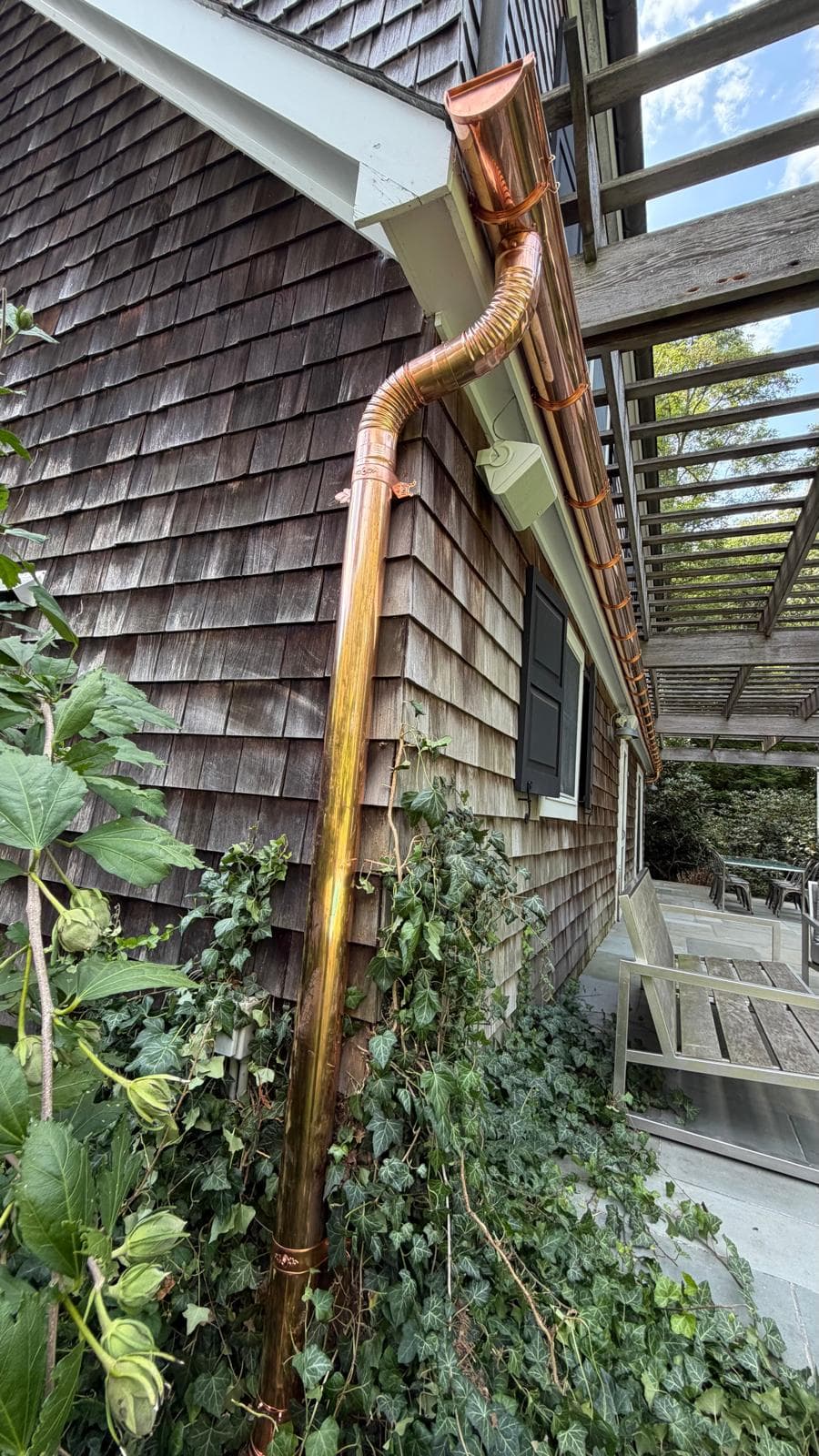 Copper downspout running down a cedar-shingled wall