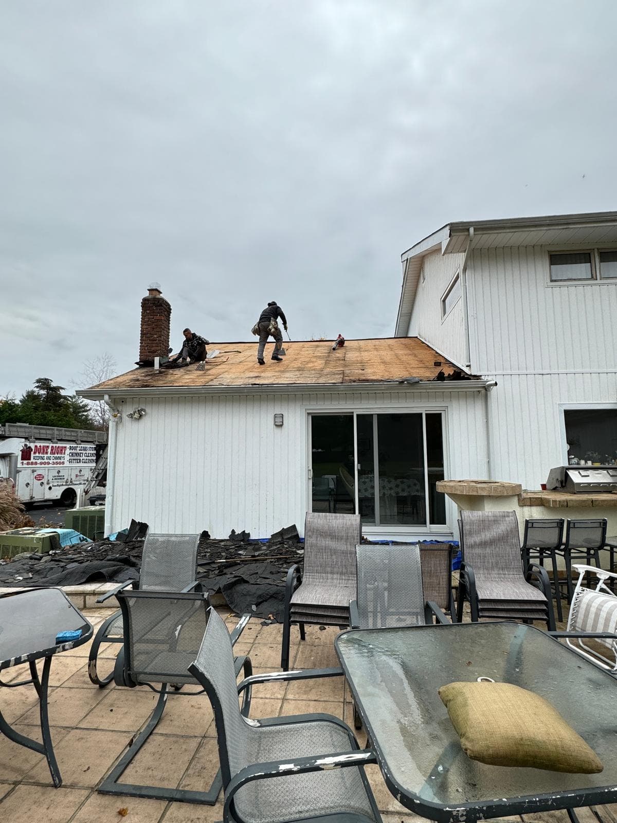 Two roofers on a ranch house roof stripped down to the wood decking