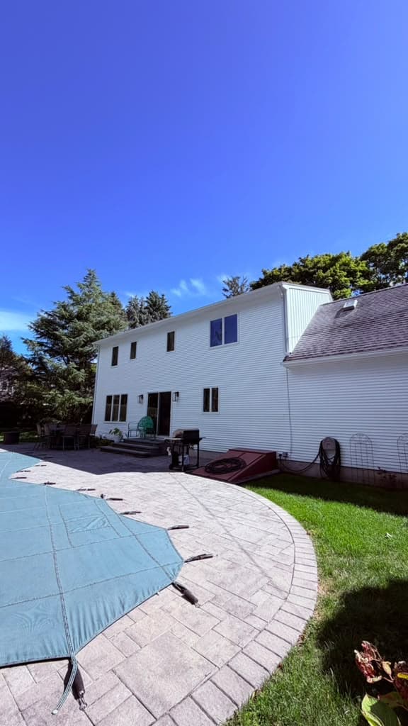 Back of a two-story house with white horizontal vinyl siding, black-framed windows and a paver pool patio